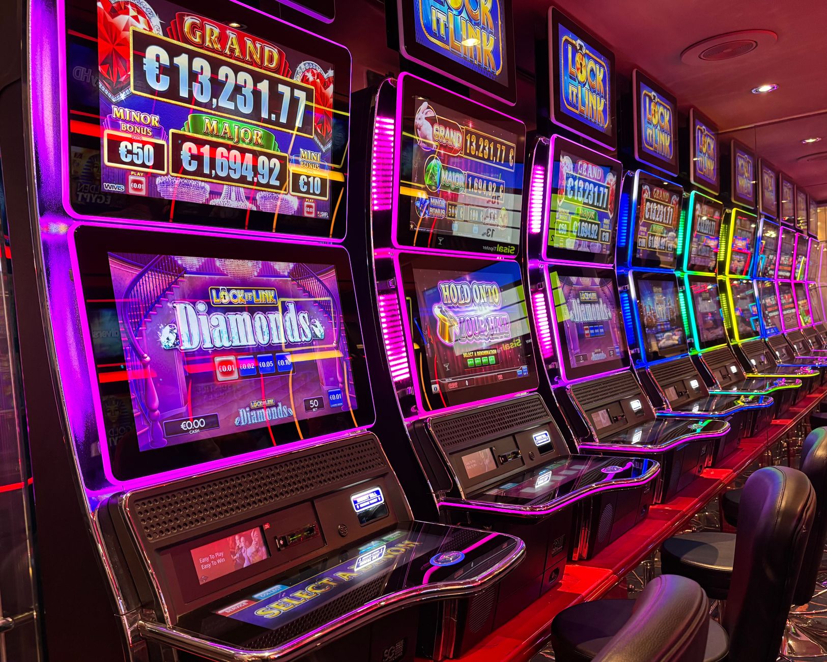 Neon ışıklar ve jackpot gösterileriyle dolu bir kumarhanede sıralanmış rengarenk slot makineleri.